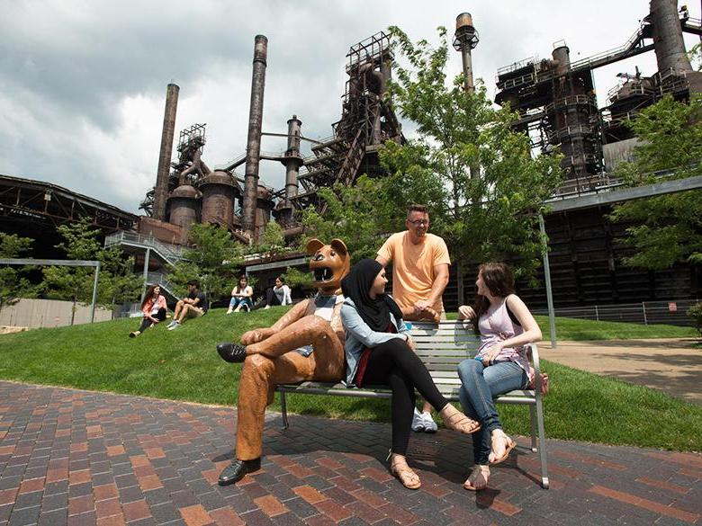 students hanging out in front of the steel stacks on the nittany lion bench